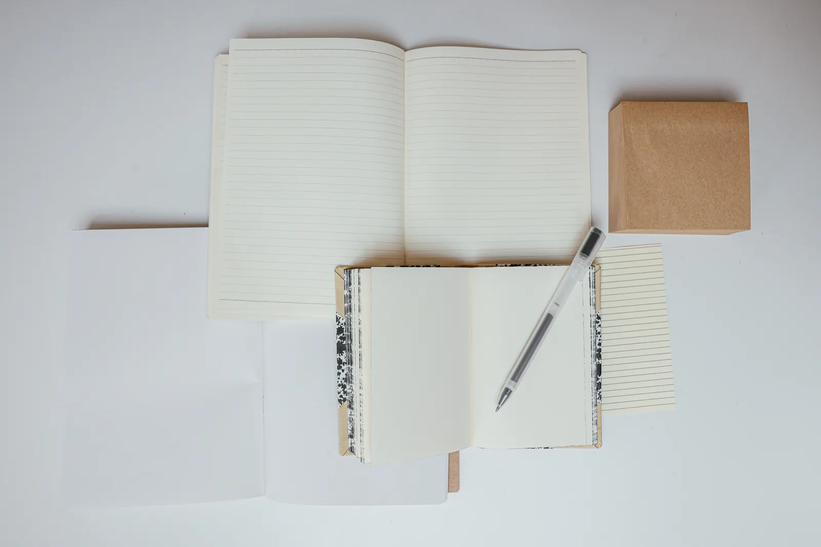 Unbranded notebooks, paper and a pen arranged on a white surface.